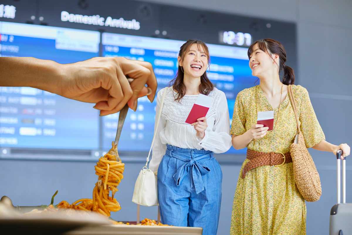 donne sorridenti in aeroporto e mano con forchetta e spaghetti