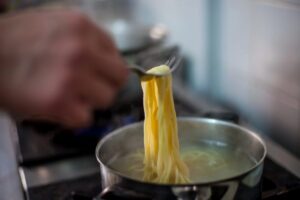 Persona che preleva spaghetti da una pentola con una forchetta