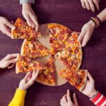 una pizza sul tagliere e le mani che prendono varie fette