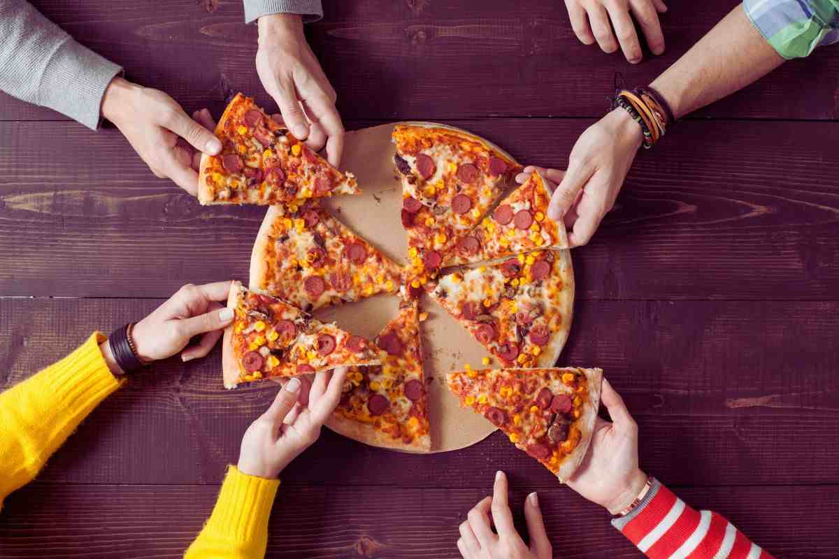una pizza sul tagliere e le mani che prendono varie fette